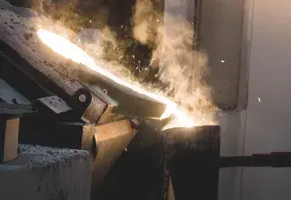 Molten metal being poured in an industrial setting, showcasing intense heat and light.