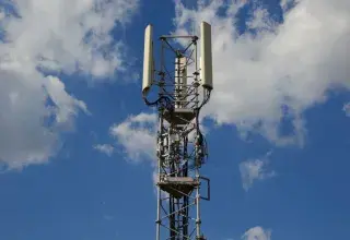 A tall cellular communication tower against a vivid blue sky, symbolizing modern technology.