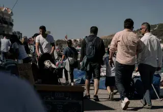 People walking through a busy street market under bright summer sunlight.