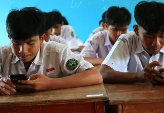 Students in uniform using smartphones in classroom