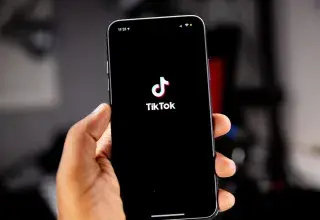 Une main tenant un smartphone affichant le logo TikTok sur fond noir