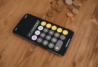 Smartphone affichant une calculatrice, avec des pièces de monnaie sur une table en bois