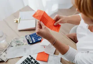 Une femme examine des tickets de caisse à côté d'une calculatrice et de billets, à son bureau