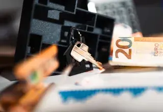 Clé de maison sur un porte-clés, billets de 20 euros et graphique sur une table