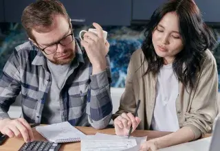 Un couple fait ses comptes à la table de la cuisine avec une calculatrice et des factures