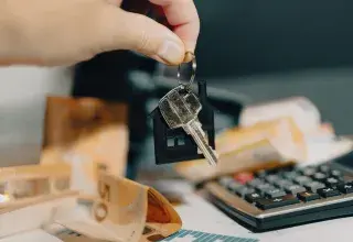 Clés d'un logement tenues au-dessus de billets en euros et d'une calculatrice